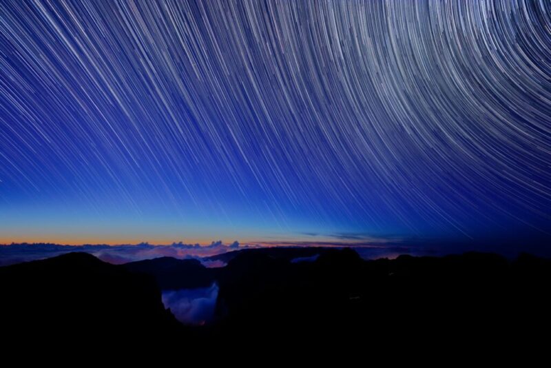 a star trail is seen in the sky above mountains